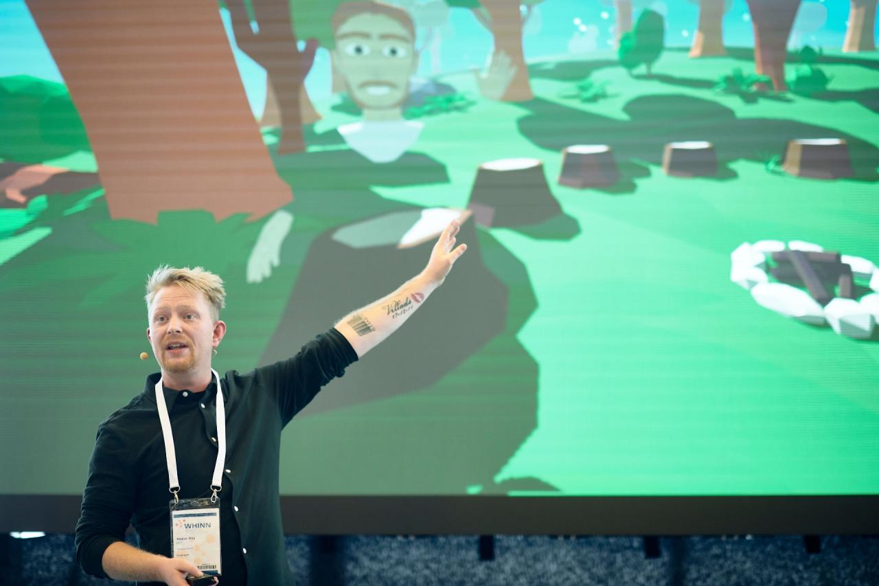 Jesper Roy Nørklit holder foredrag på WHINN foran en skærm med en virtuel verden